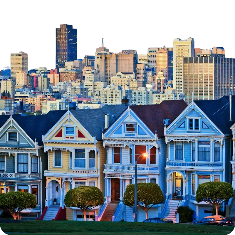 Vibrant row of Victorian Painted Ladies houses in Alamo Square, San Francisco, with the downtown skyline glowing in the background at sunset.