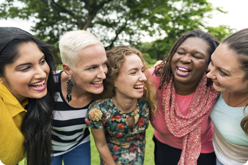A joyful group of five diverse individuals hugging outdoors with trees in the background, representing the positive impact and community support experienced by transgender patients after gender-affirming surgery at ART Surgical.