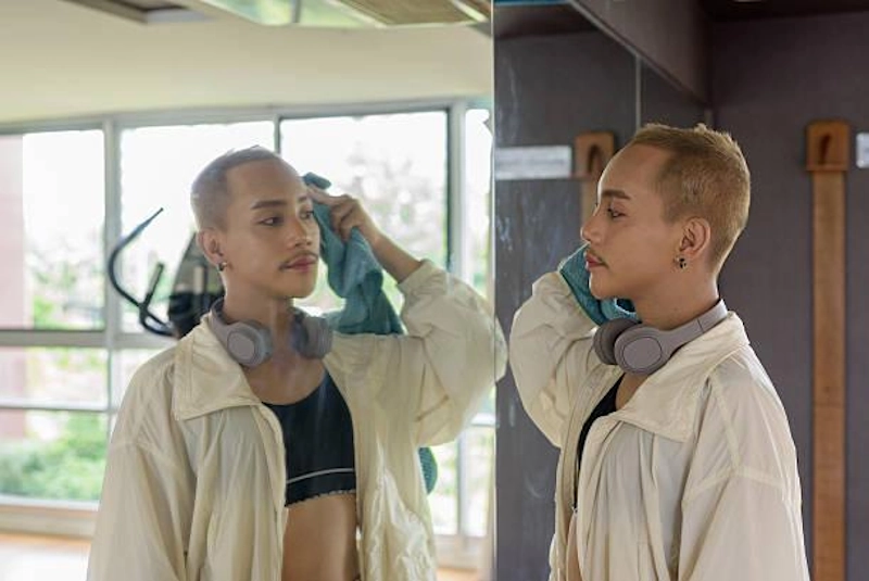 A person looking at their reflection in a gym mirror, illustrating the process of relearning how to see yourself and improving body image after gender transition.