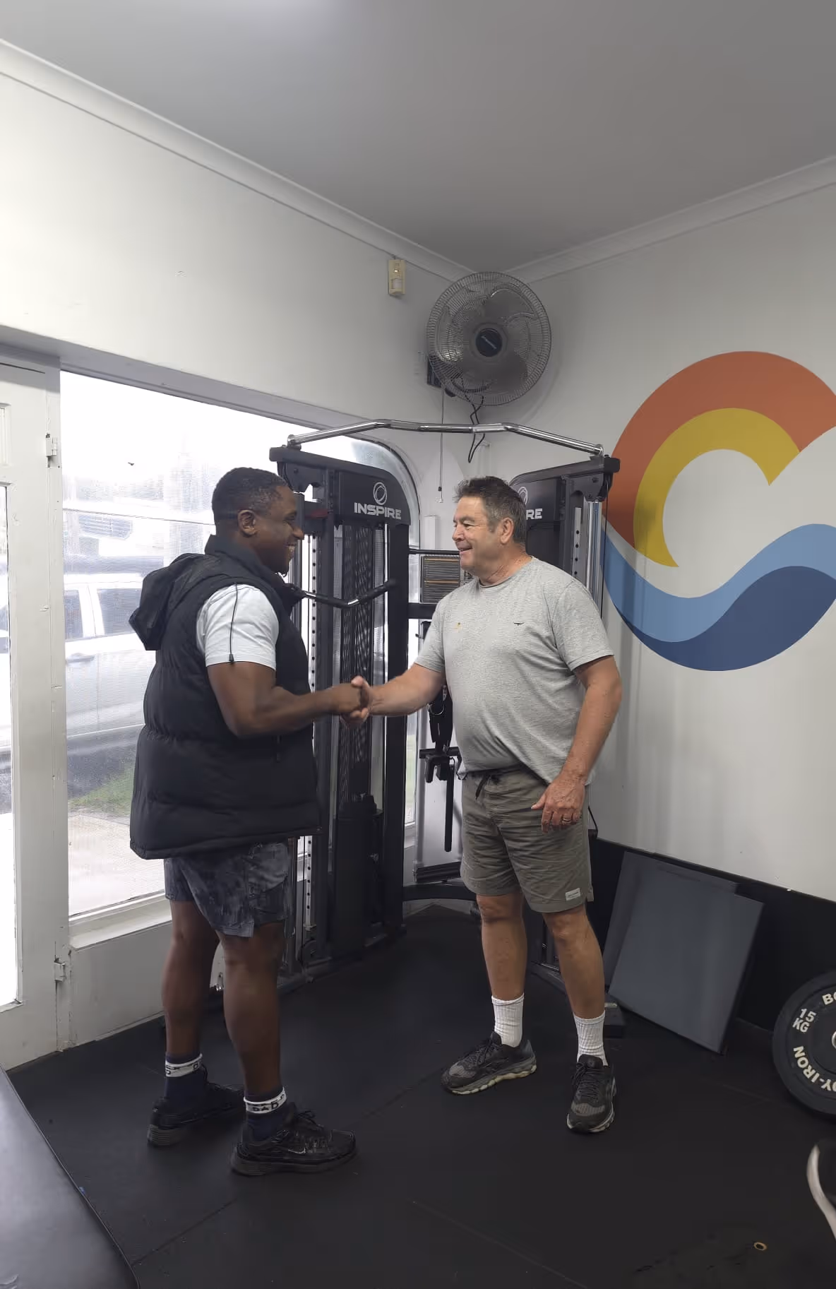 Trainer Akeem shaking hands with a gym member and smiling at Coastal Bodies fitness studio.