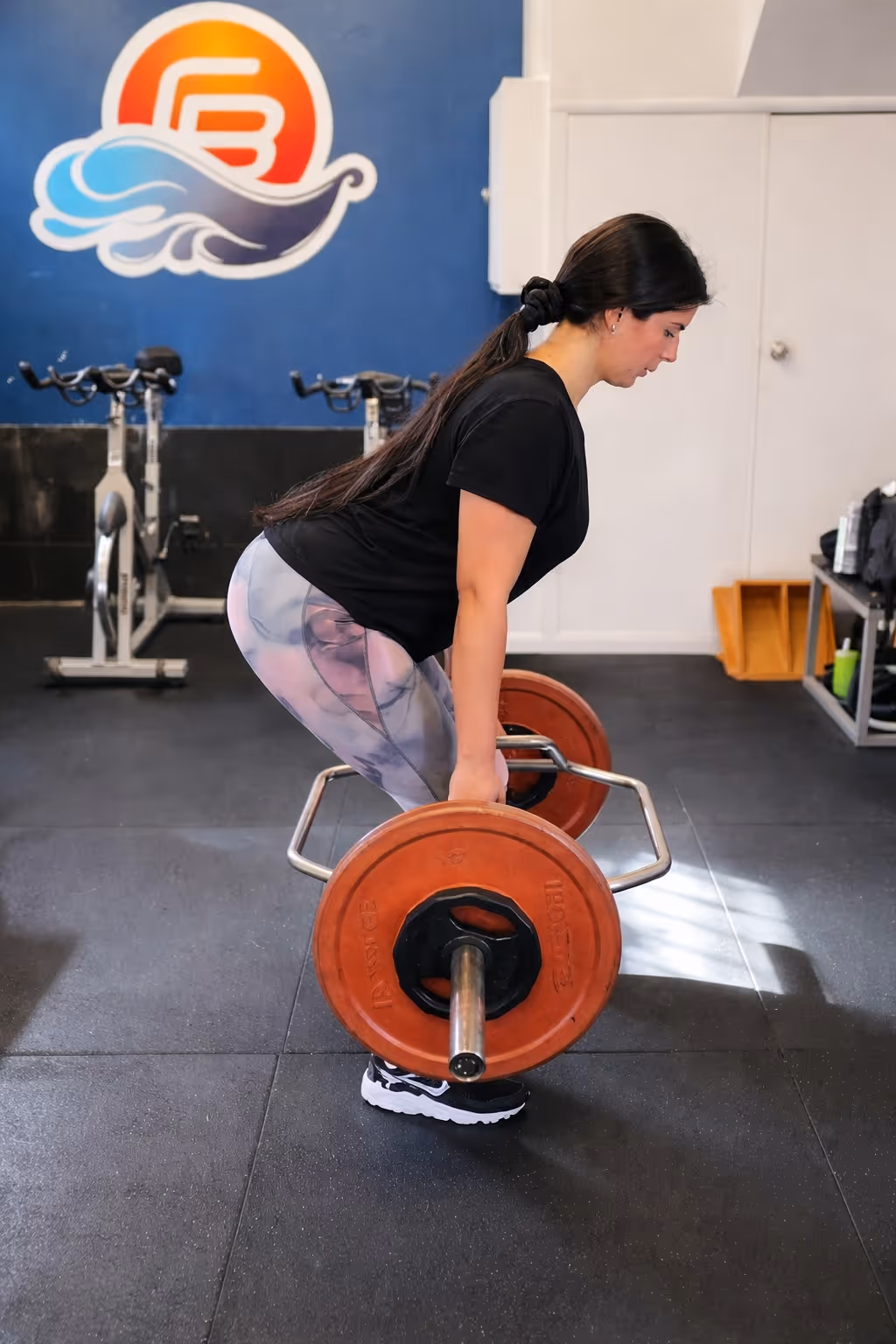 Woman performing deadlift exercise with a barbell in Coastal Bodies fitness studio.