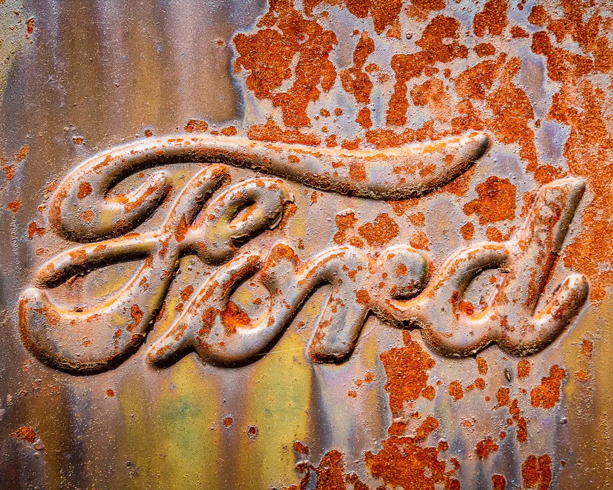 close up of rusted Ford insignia on antique car