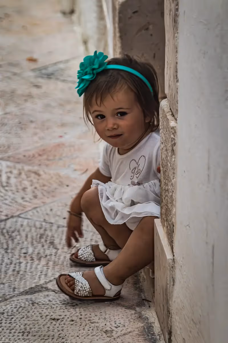 Italy- little girl with green headband sitting in a doorway peeking out