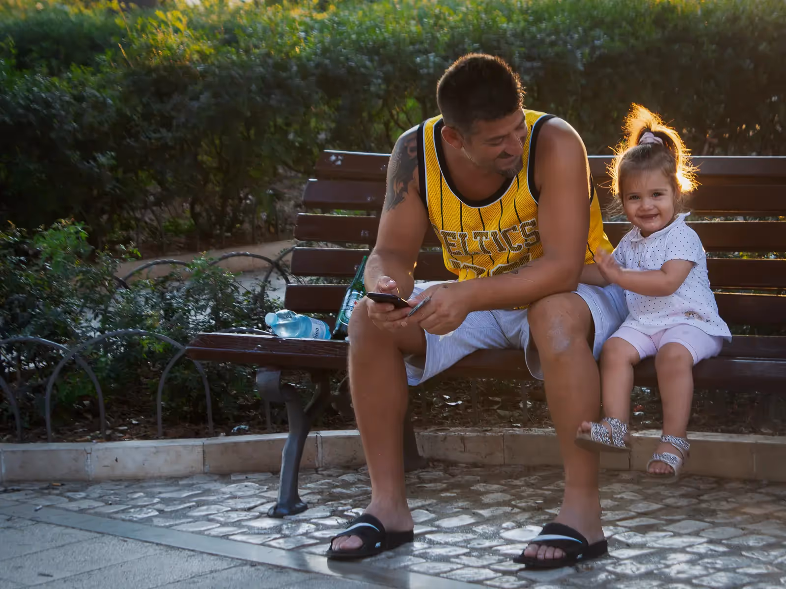 Italy: father and young daughter sitting on a bench with the sun creating a halo behind the girl