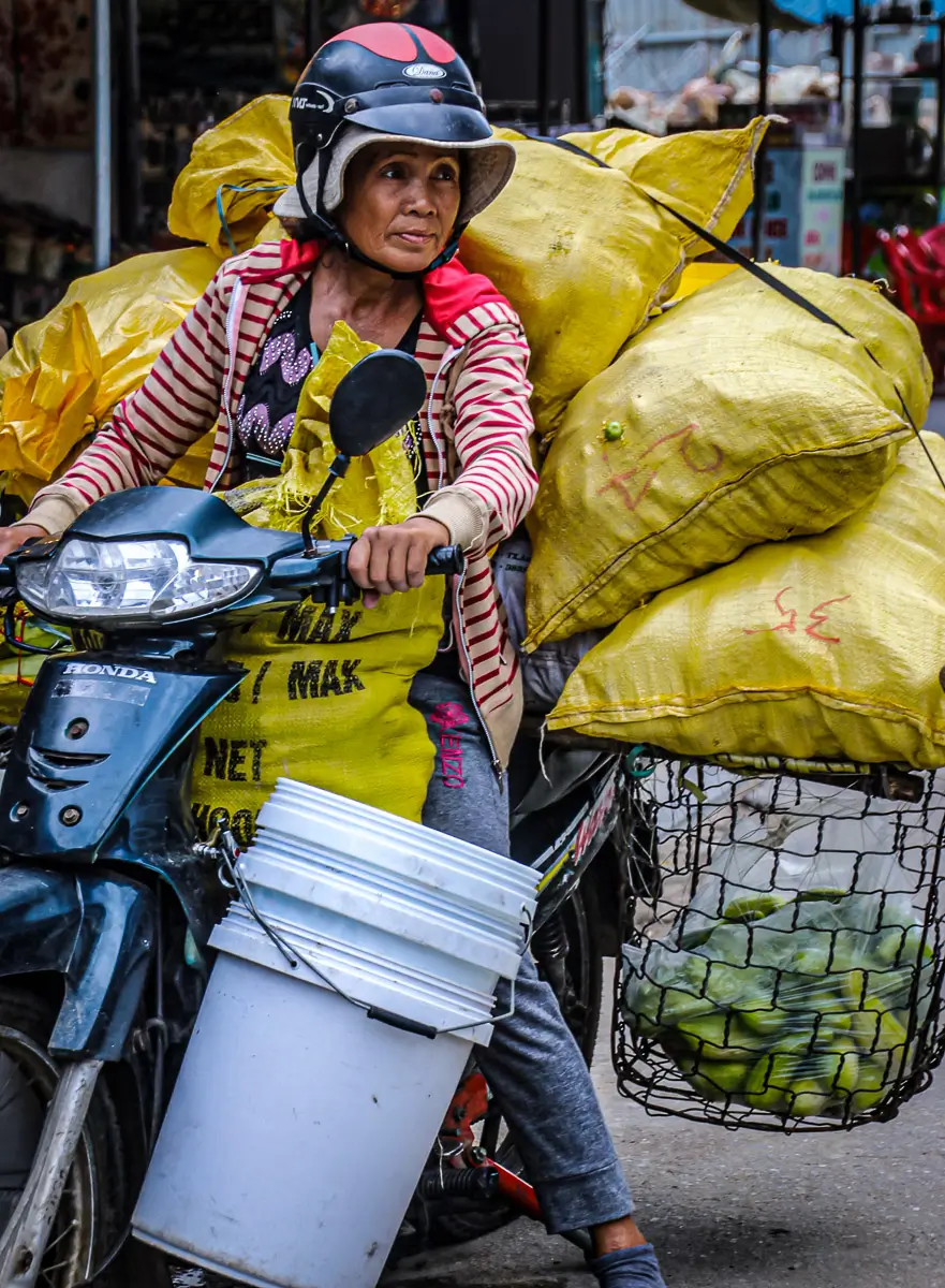 Vietnam: woman on moped carrying an impossible number of bags