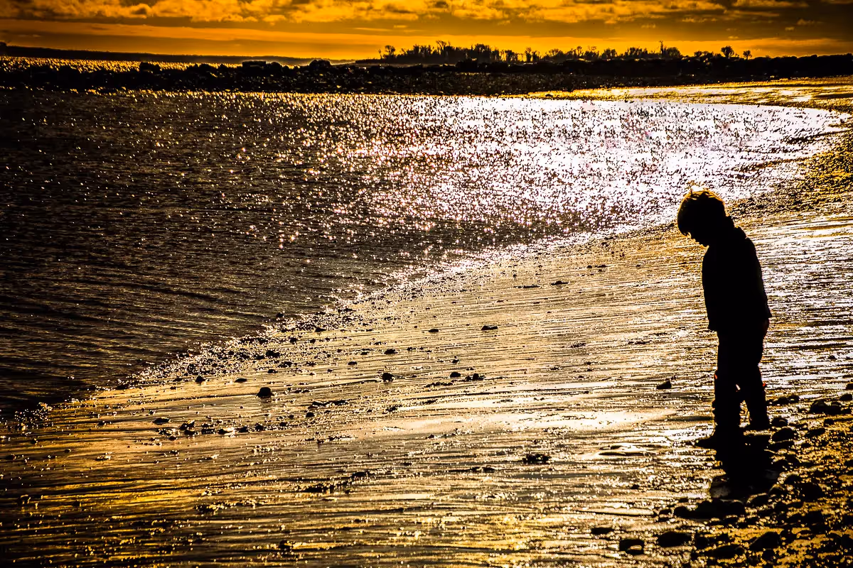boy standing by the waters edge at sunset in Westport CT