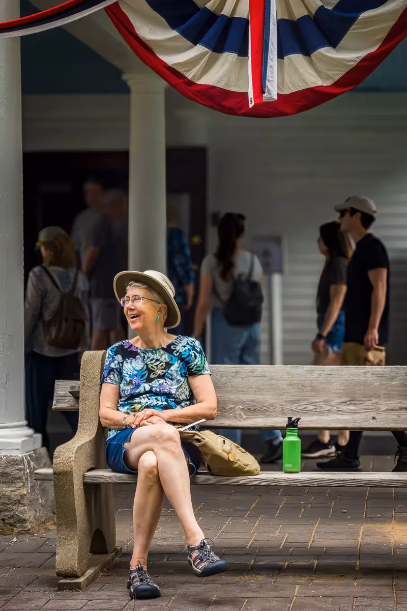 2024 Haddam Neck Fair: lady in hat sitting under curved american flag