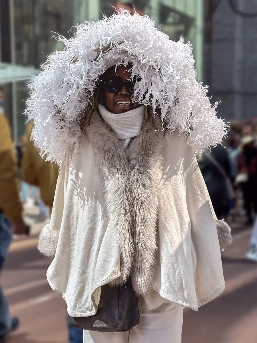 2024 Easter Bonnet Parade, NYC:  Woman with off white shawl and huge head cover hanging down to her shoulders made of shredded paper