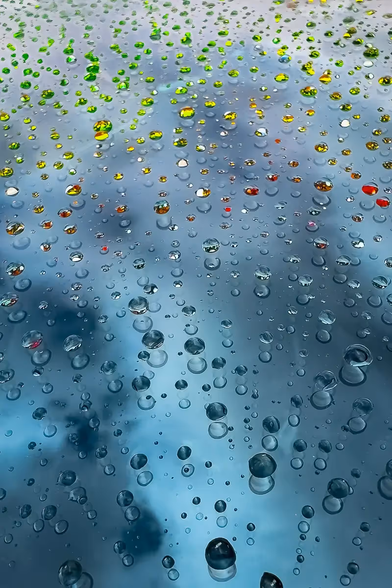 water drops in different colors from reflections of the background, on the hood of a car. 
