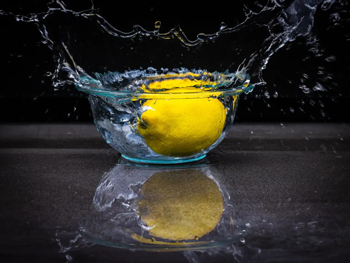 Water splashing out of glass bowl from lemon dropping in