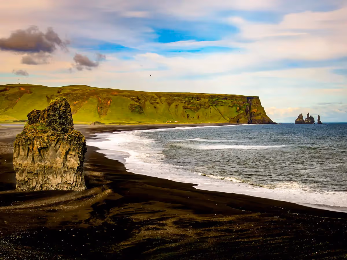 Black Cove in Iceland: black Water surrounded by a curved black sand beach, large rock formations and green cliffs