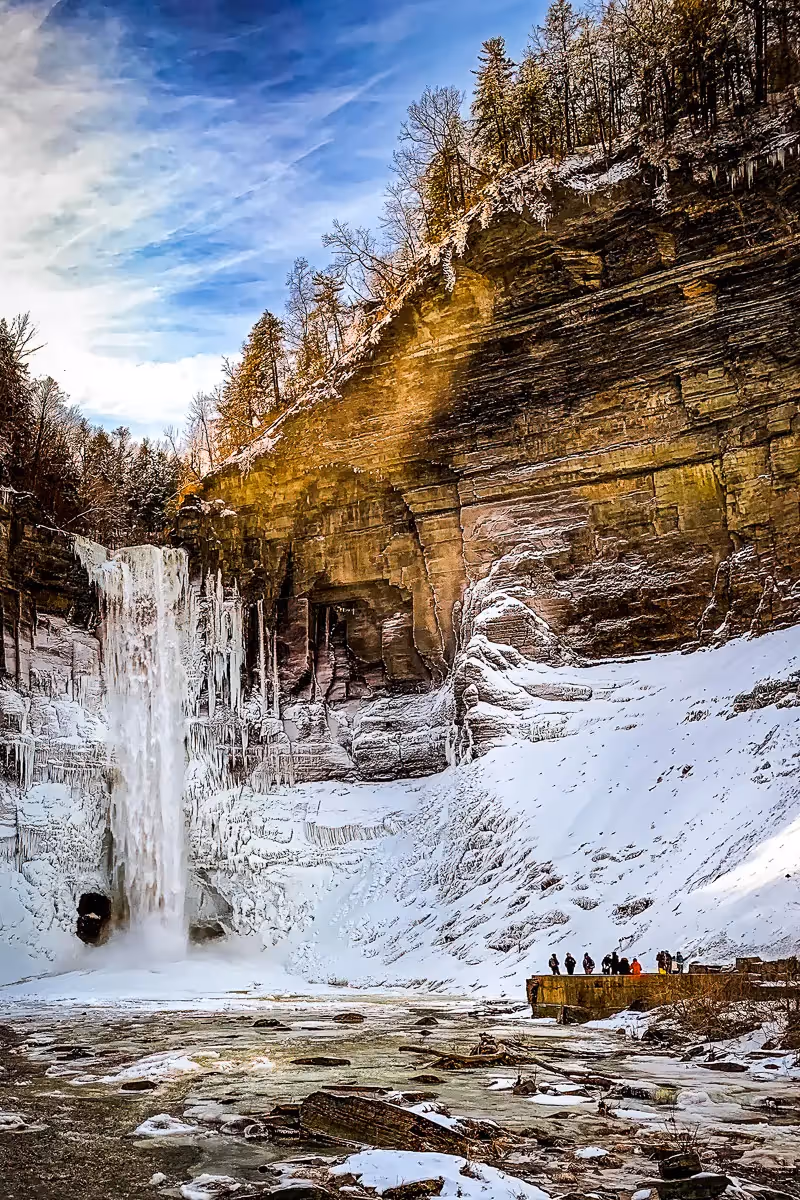 A small crowd of people show the scale of the enormous frozen waterfall between tall cliffs in Ithaca, NY