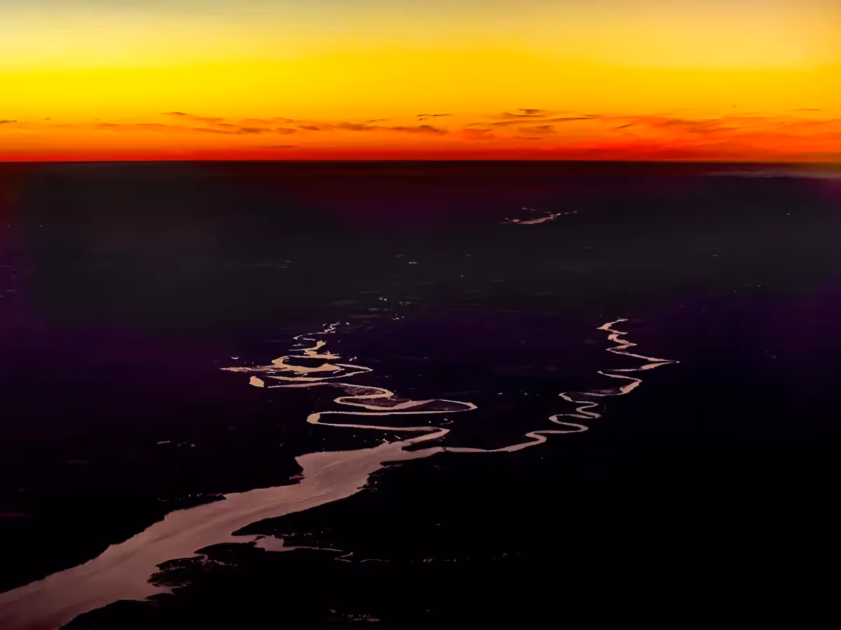View from airplane window of tributary fork with sunset in the distance