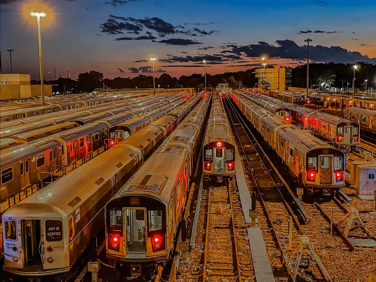Parked subway trains in various length lines are lit up by the sunset sky