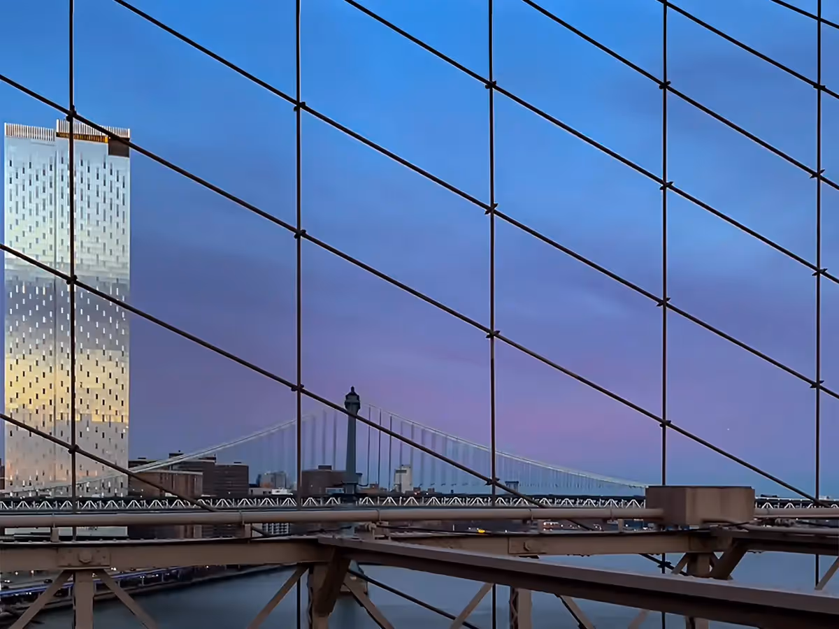 Looking through the wires on the side of the Brooklyn Bridge to see the water, buildings and the next bridge