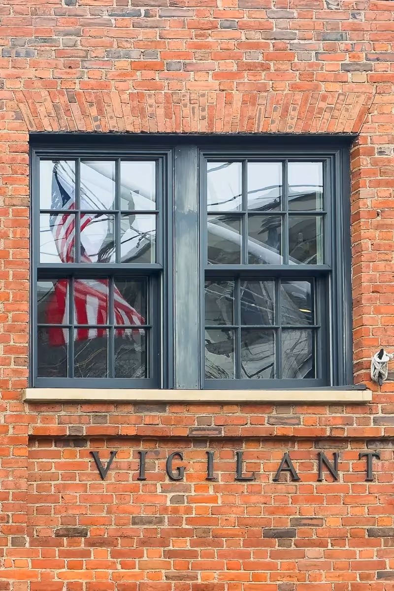 Reflection of the American Flag through a window on a brick building with the word: Vigilant on it