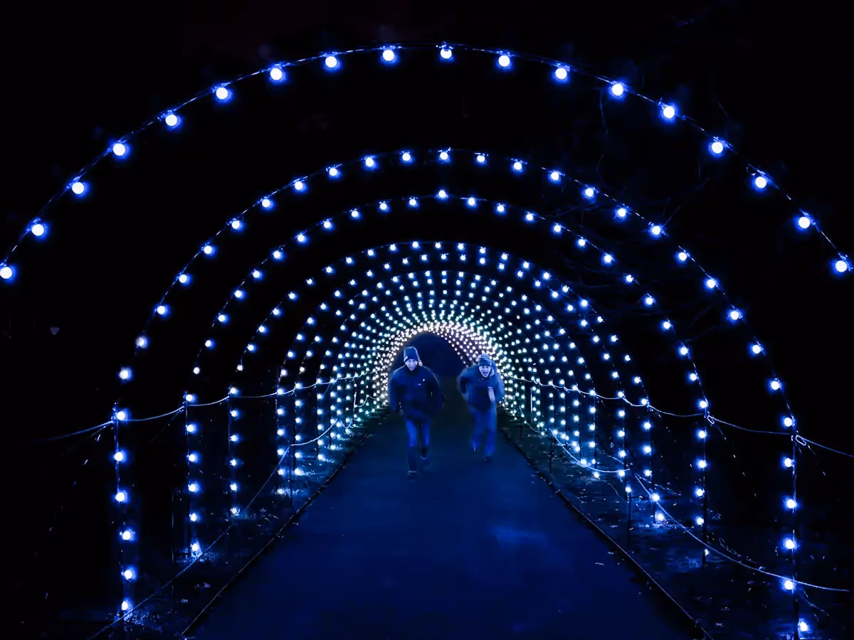 2 men running towards me through a series of lit half circles of lights that recede in the distance