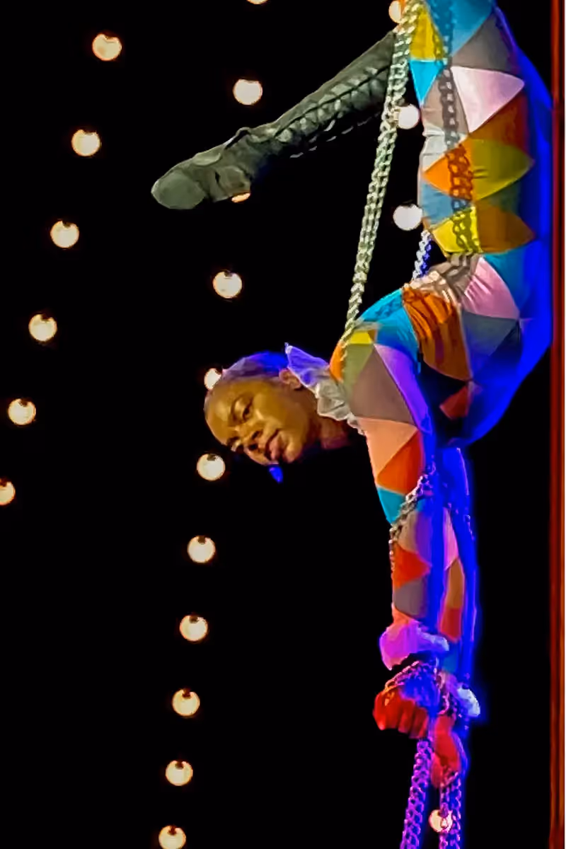 Upside down trapeze artist hanging in the air among the hanging lights