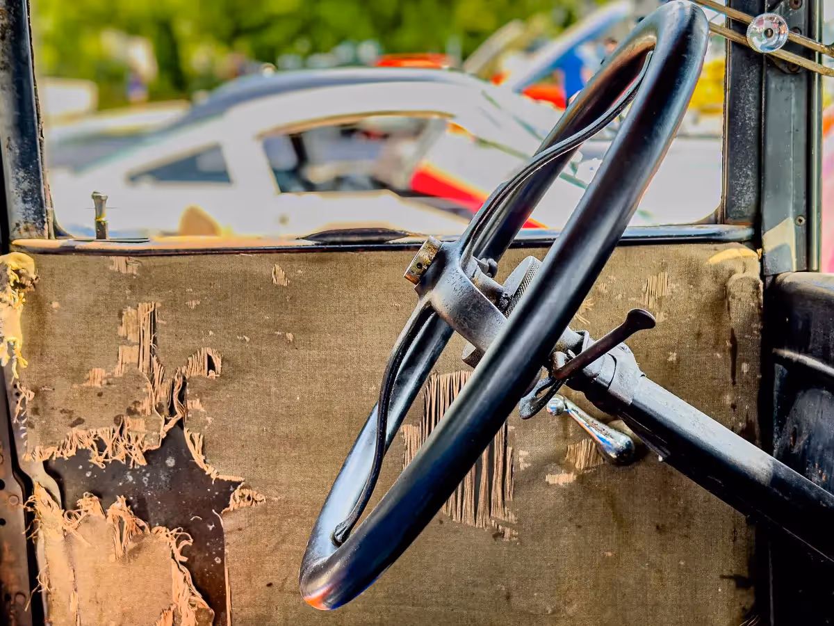 Norwalk, CT car show:  from the inside of an antique car showing ripped fabric on the door and and old drivers wheel