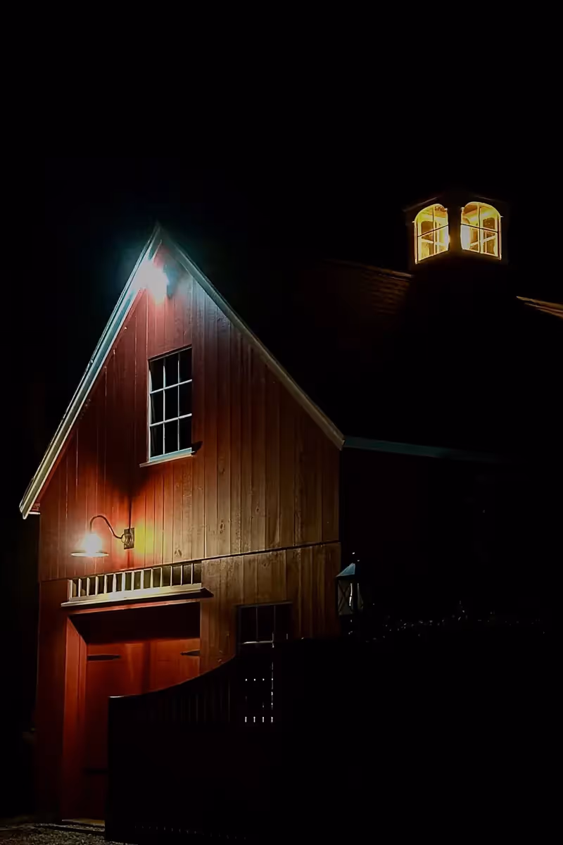 the red barn and single lit cupola shines light in the pitch black night