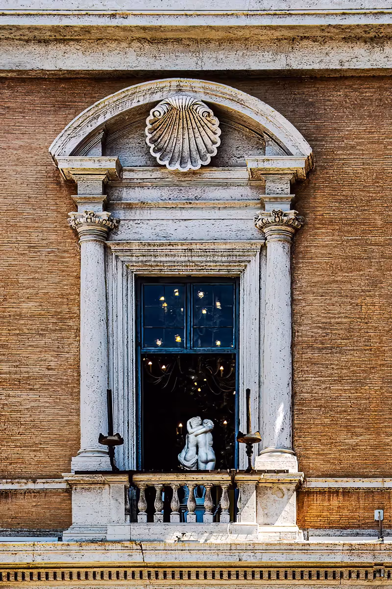 Looking up through a window in Italy, at a sculpture of 2 nude, huging busts from behind and  sparkling lights in the black background