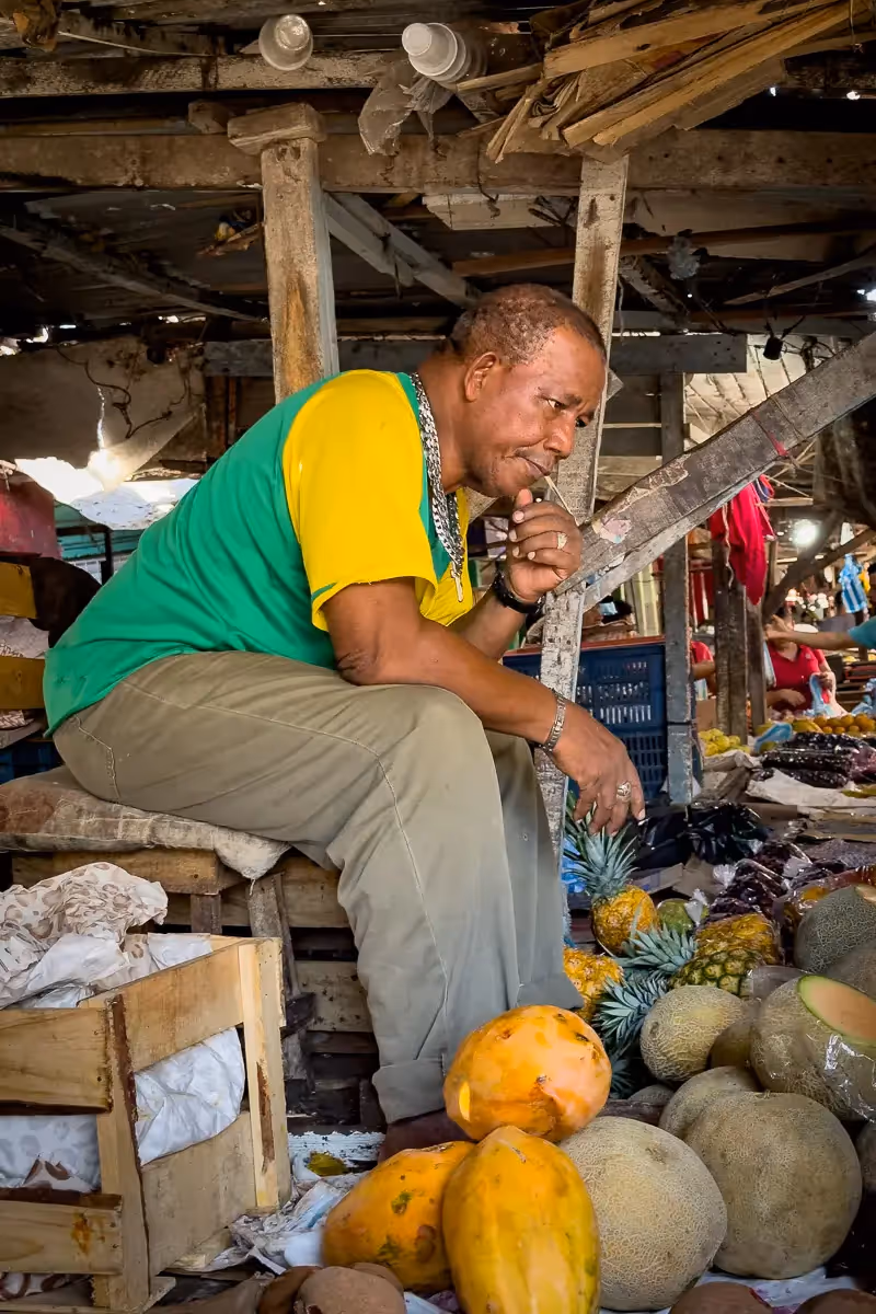Colombia Market fruit seller sitting on crates on top of his fruit table, waiting for customers