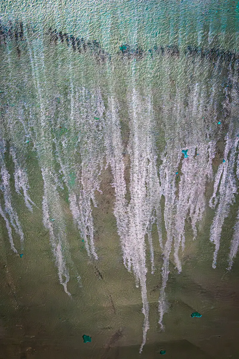 Patterns of rust and barnacles on the hull of a boat out of water.