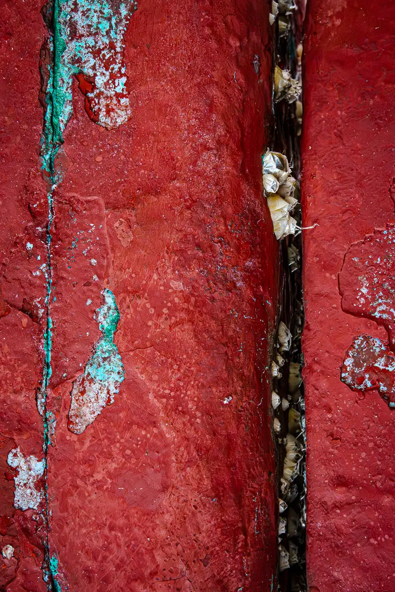 Patterns of rust and barnacles on the hull of a boat out of water.