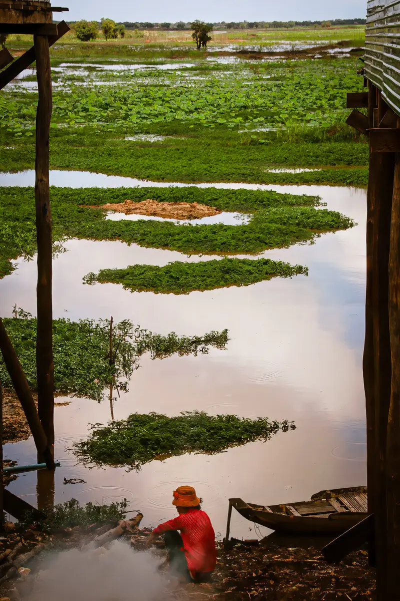Cambodia: man sitting on the edge of a river with a part of his wooden boat in view