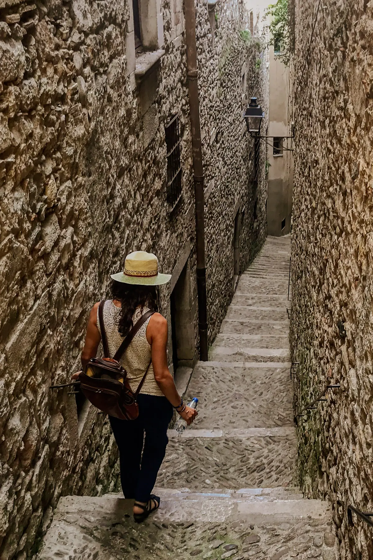 Spain: Woman with hat walking down stone steps through an narrow alley of stone buildings