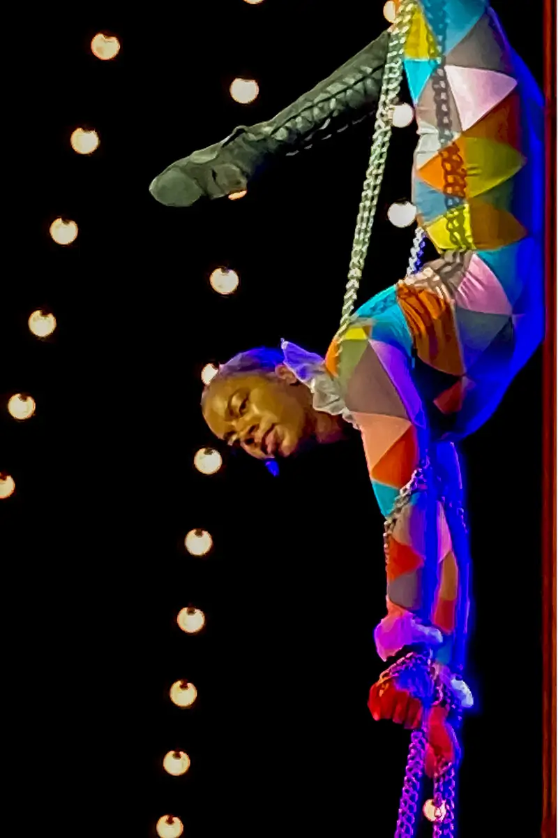 Upside down trapeze artist hanging in the air among the hanging lights