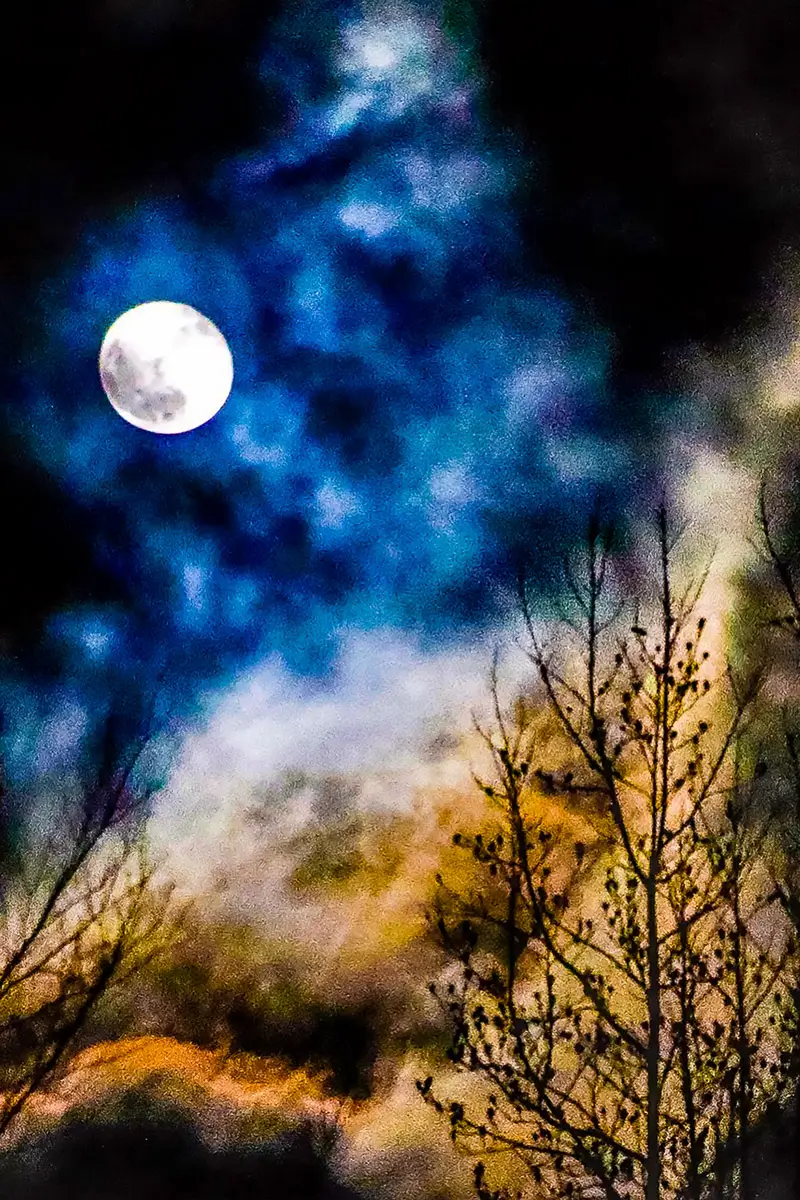 Painterly looking photo showing the moon through a dramatic, dark sky