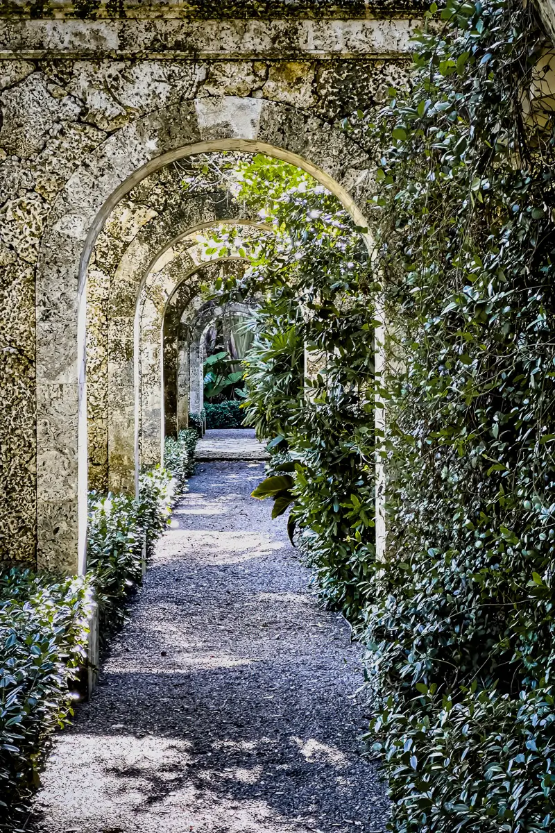 Pathway of multiple stone archways covered  in plants on one side