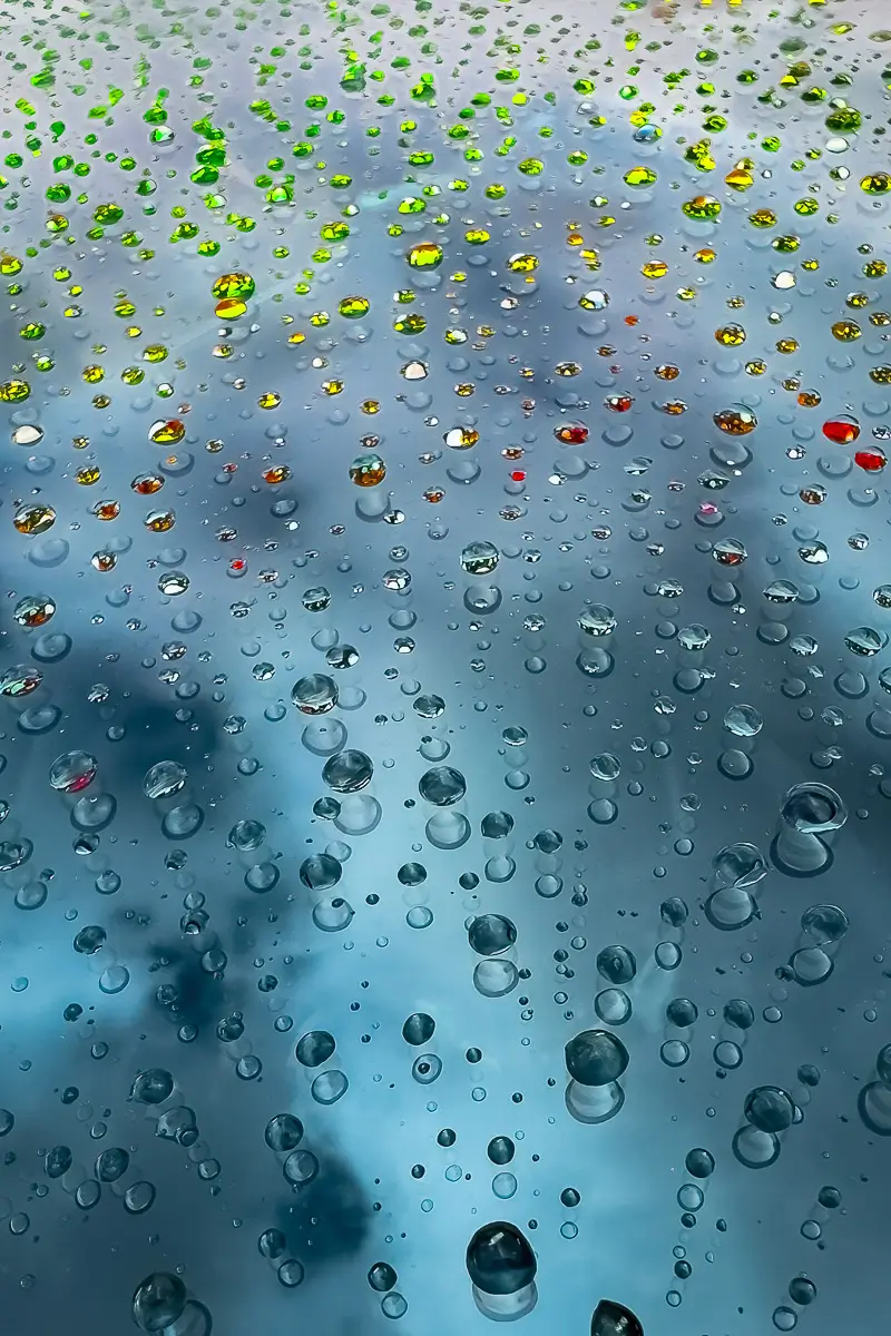 water drops in different colors from reflections of the background, on the hood of a car. 