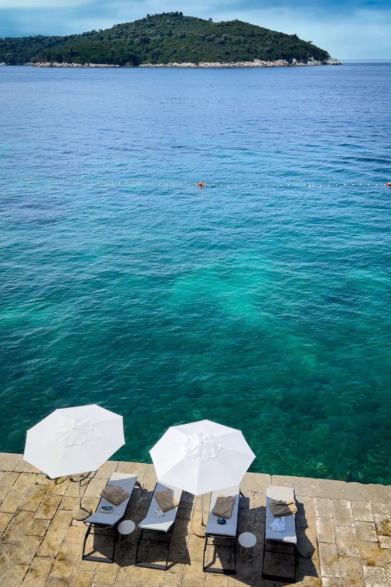 Dubrovnik, Croatia: 2 chaise lounge chairs with umbrellas and towels waiting for vacationers to relax overlooking the beautiful serene sea with an island in the distance 