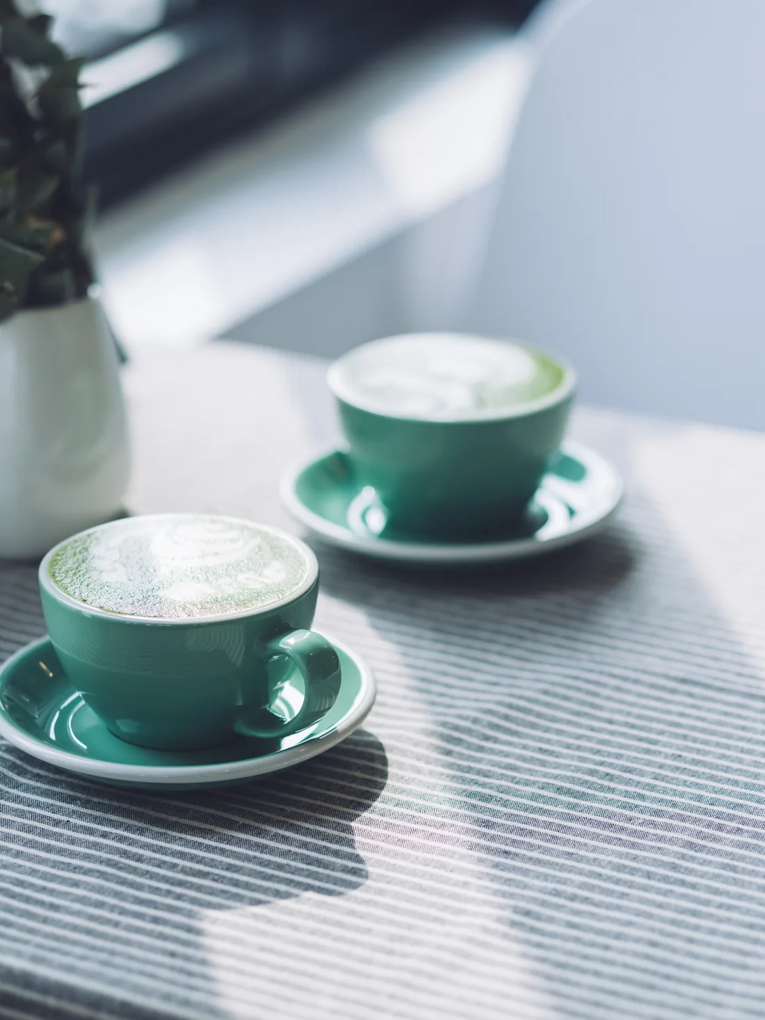 Two green cups of latte on a striped tablecloth