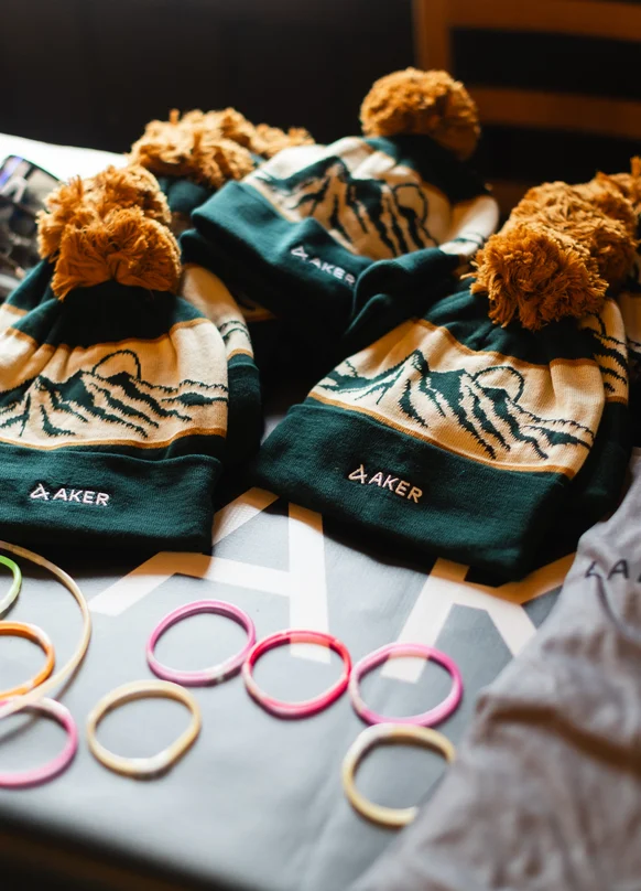Green Aker beanies with orange pom-poms laid out on a table