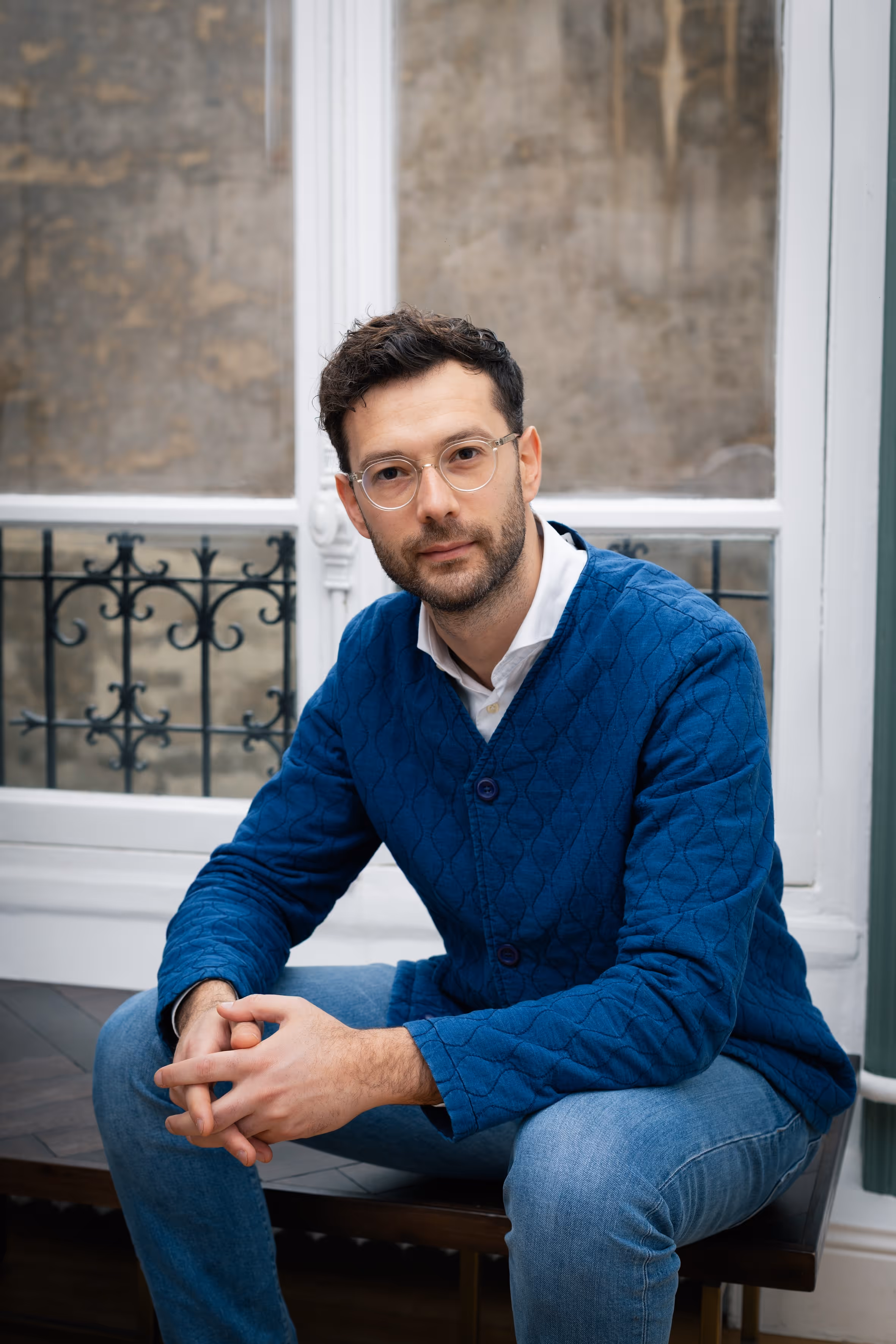 A portrait of a man wearing eyeglasses, sitting and smiling.