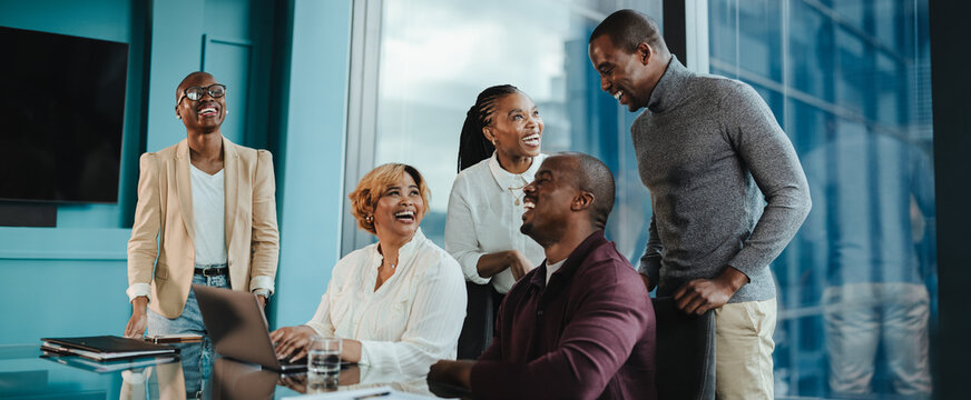 Five diverse colleagues smiling and talking together in a modern office conference room.