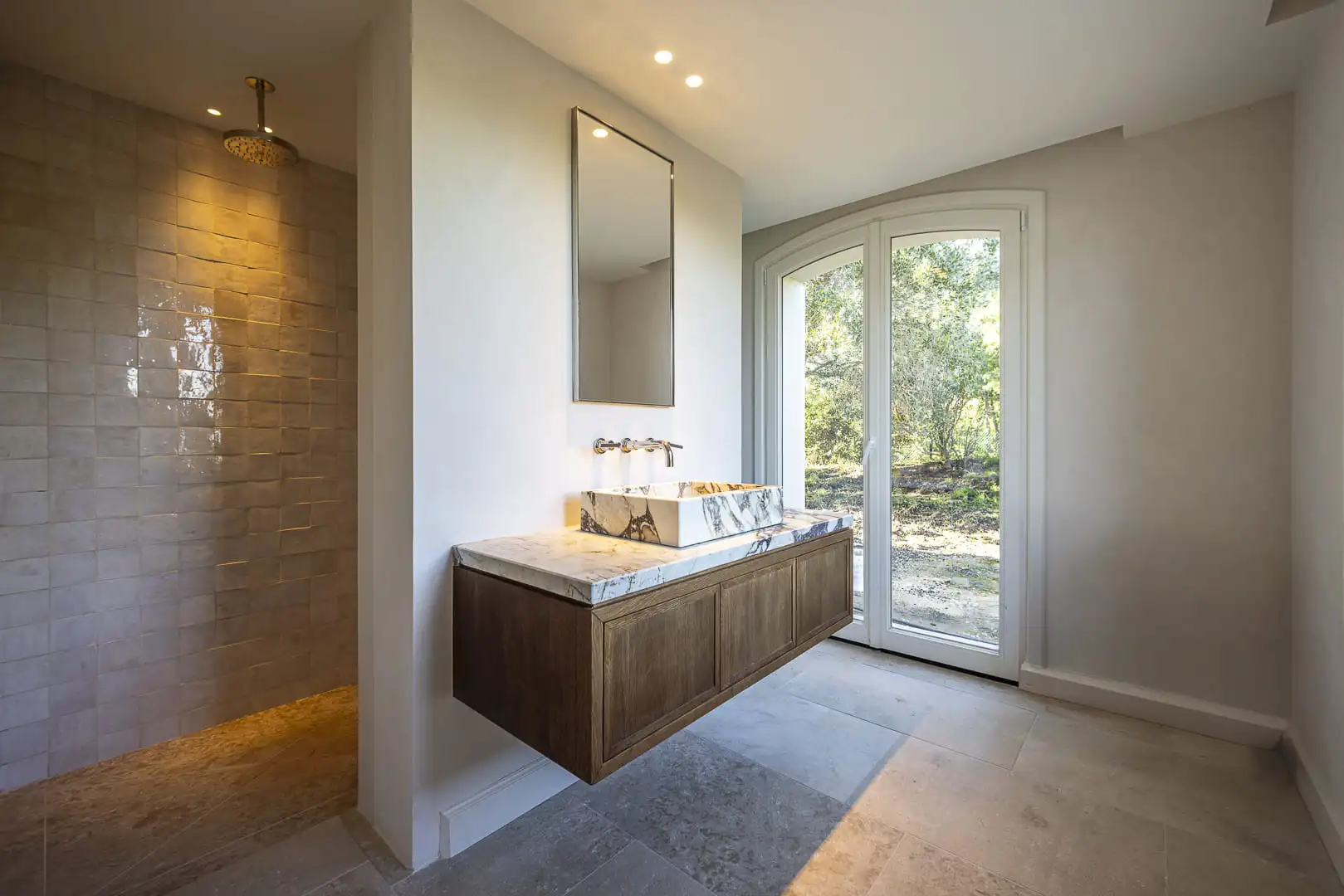 Salle de bain contemporaine avec meuble vasque suspendu en bois et marbre, douche à l’italienne et ouverture vers le jardin.