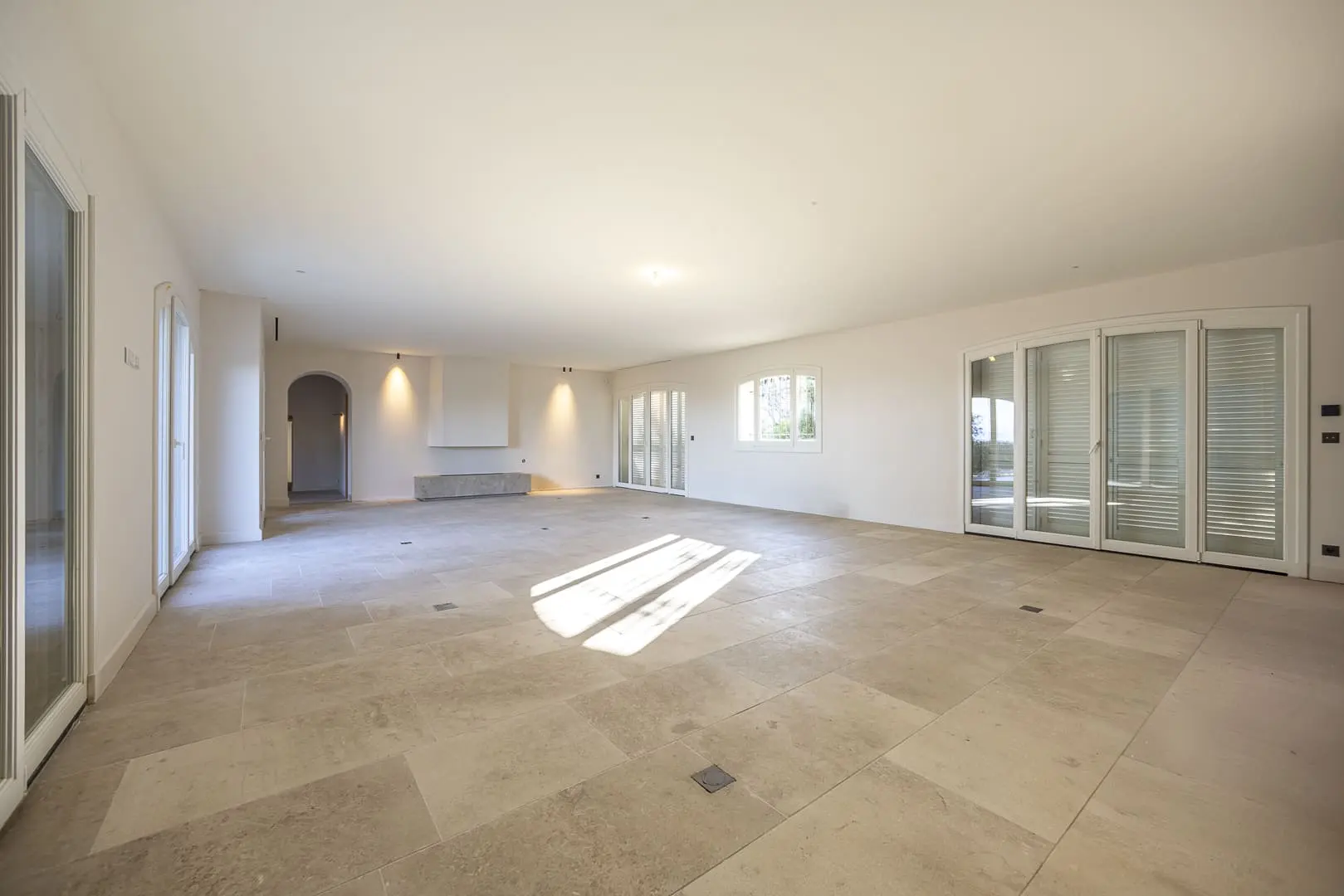 Séjour lumineux achevé avec sol en pierre naturelle, murs blancs et menuiseries extérieures laissant entrer une lumière abondante.