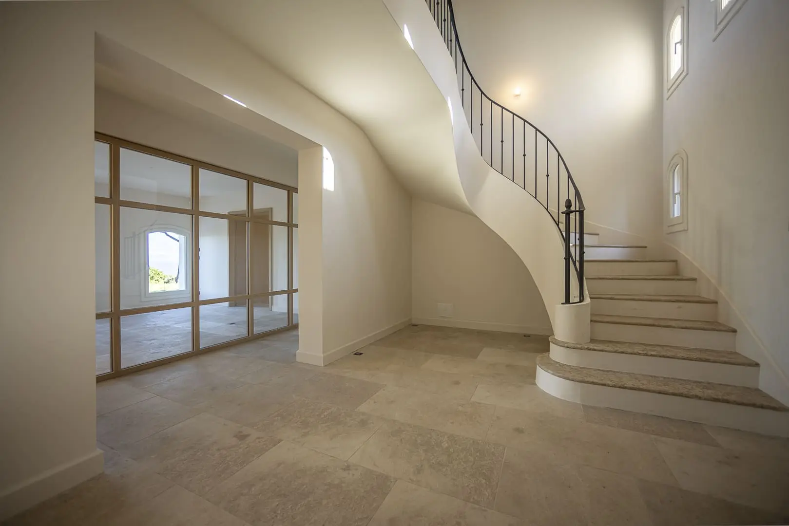 Escalier courbe habillé en pierre naturelle avec garde-corps en ferronnerie noire dans un hall lumineux.