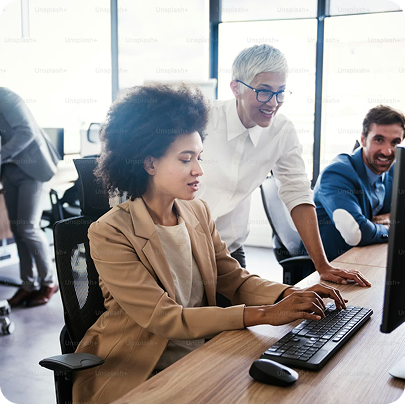 Colleagues collaborating at a desk with one woman typing on keyboard and another standing and smiling.