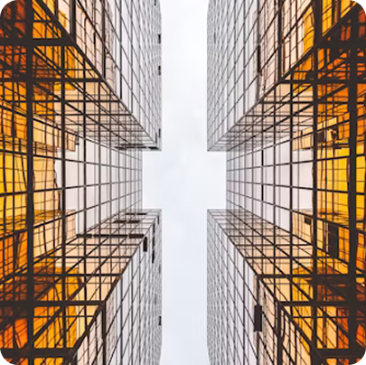 Upward view of four modern glass skyscrapers with orange reflections against a cloudy sky.