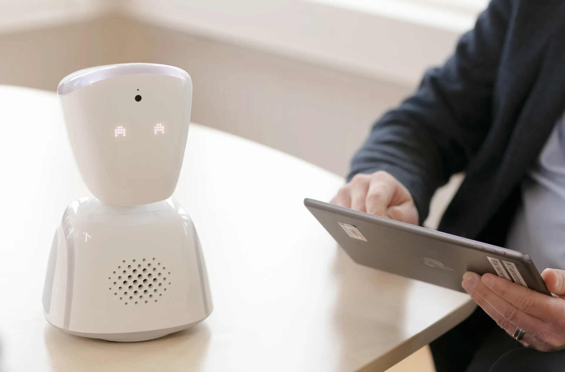 Three girls smiling and holding up an AV1 robot. They are outside in a school playground