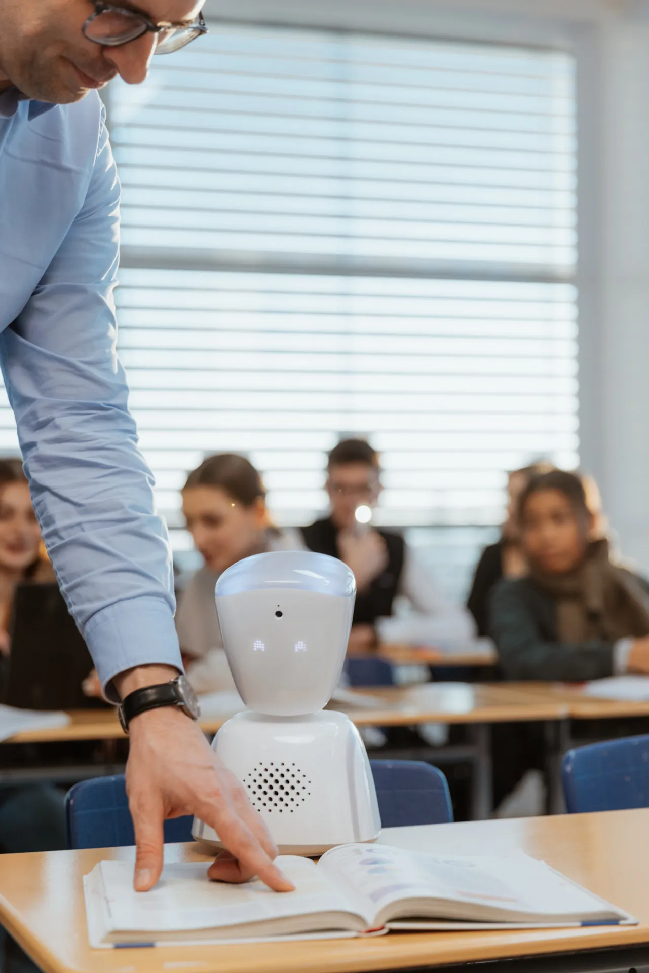 AV1 robot, a girl and 3 boys are in the classroom who are learning and 1 of the boy is raising his hand to speak.