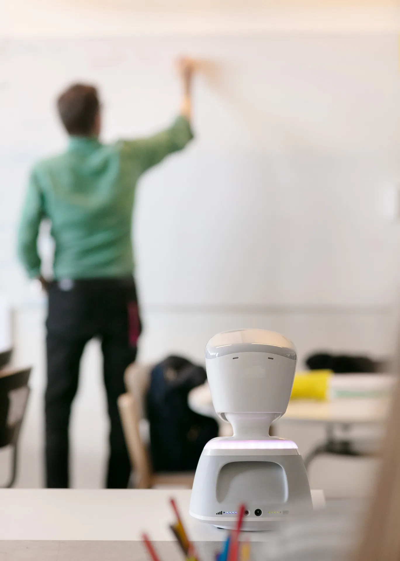 AV1 robot, a girl and 3 boys are in the classroom who are learning and 1 of the boy is raising his hand to speak.