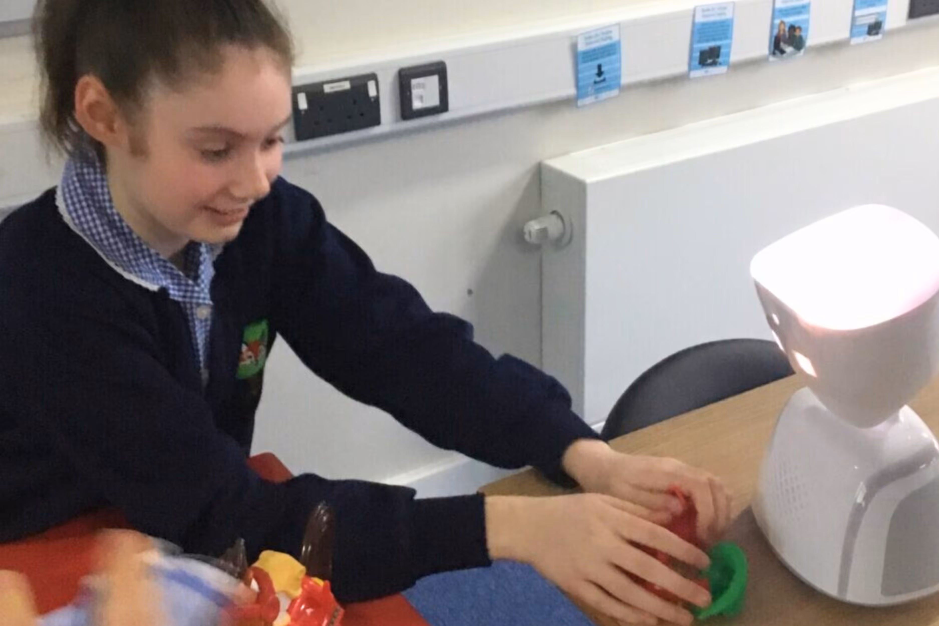 A student playing with an AV1 Robot on a desk. She's wearing school uniform and is in a classroom.