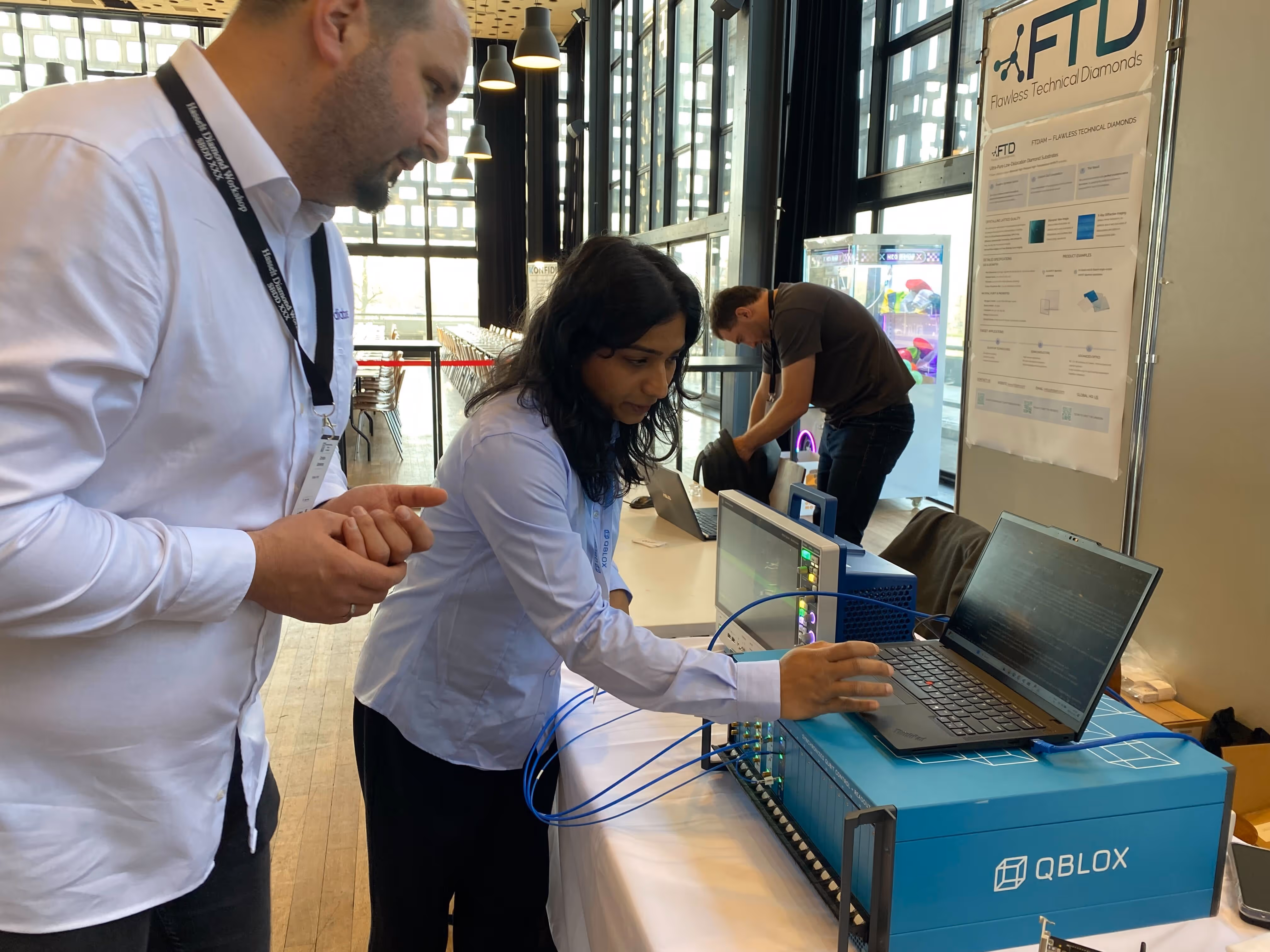 Two people interacting with a laptop and the Qblox Cluster on a table at a tech event,