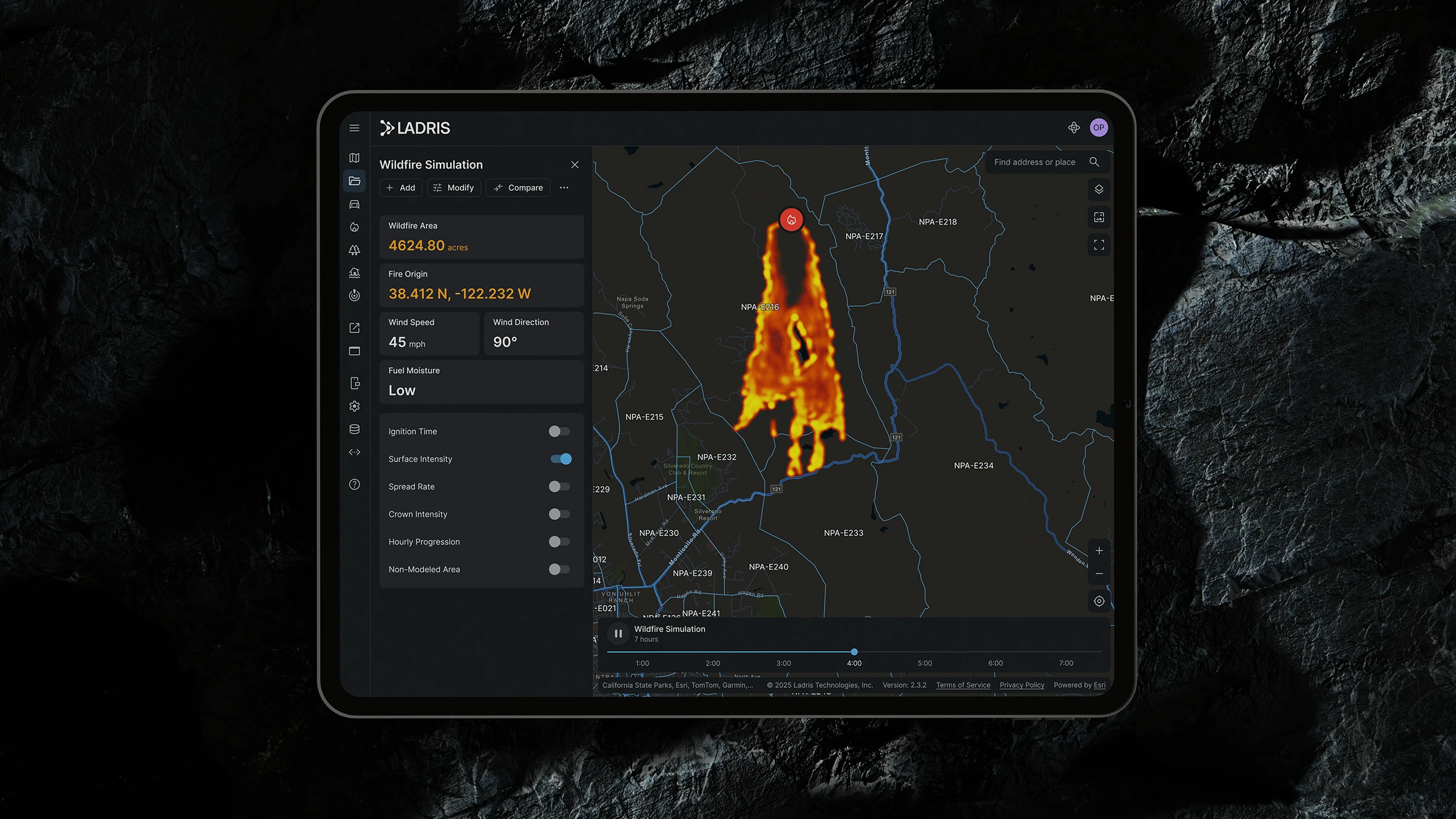 Tablet screen showing LADRIS wildfire simulation with a fire map, details of wildfire area, fire origin coordinates, wind speed and direction, and simulation controls.